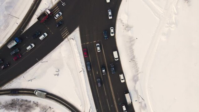 Bird's eye view of a snowy city crossroads with cars in winter. Vehicles drive and stand at a traffic light. Regulated intersection, interchange. City of Vladimiro, Lybidskaya highway. UHD 4K.