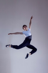 Fototapeta na wymiar One Professional Caucasian Male Ballet Dancer Performing in Flight With Hands Outspread in Studio