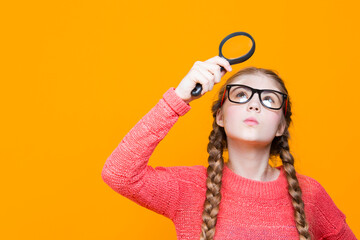Calm Intelligent Caucasian Girl in Glasses And Coral Knitted Sweater Holding Big Magnifying Glass...