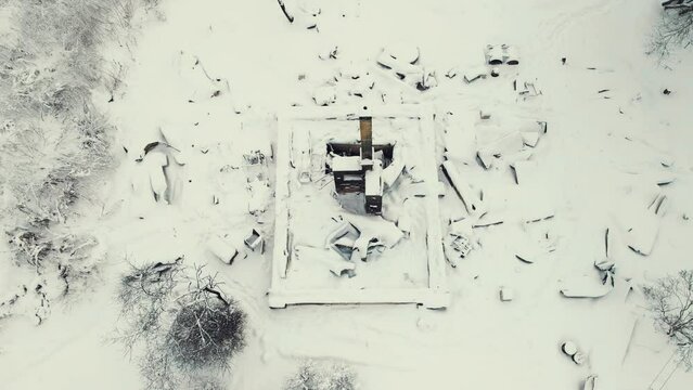 Aerial view of a destroyed stove in winter, a tall chimney sticks out. War, a bombed-out house, a consequence of the bombing, rocket attacks. Snow-covered ruins abandoned by people. UHD 4K.