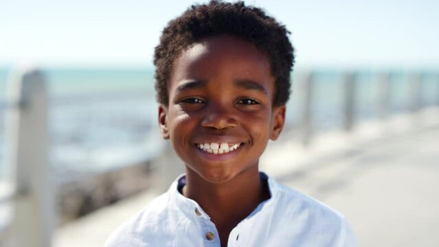 Black child, face and smile for happiness on a beach promenade while on summer travel vacation for fun, freedom and adventure outdoor. Portrait of boy kid from France showing teeth on holiday at sea