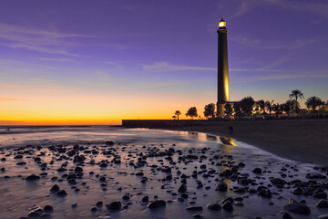 Travel Destinations. Lighthouse of Maspalomas At Gran canaria Island Known as Faro de Maspalomas at Sunset During Blue Hour With Sea And Stones.