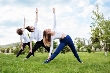 Teens with instructor practice yoga outdoors standing on grass making stretching. Maintaining healthy lifestyle