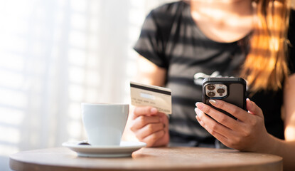 Beautiful Asian woman using smartphone and credit card to make online purchases in cafe shop.