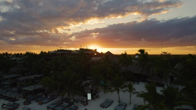 Aerial view of the sun setting behind the tulum landscape in Mexico while tourists walk over the Akiin Beach.