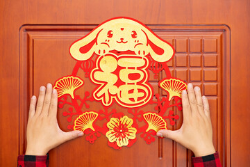 man sticking a Chinese New Year of Rabbit decoration to a door at horizontal composition translation of the Chinese word is fortune no logo no trademark