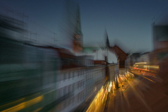 Just before closing time in Lübeck, people go shopping in the illuminated street, while the city already disappears in the coming night, multiple long and short exposure, abstract art image
