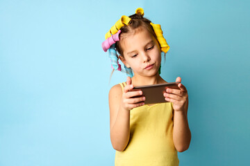 Little girl with curlers on blue background with copy space