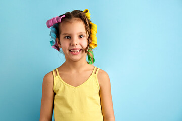 Little girl with curlers on blue background with copy space