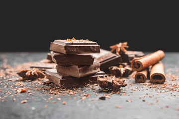 Dark chocolate bar pieces on dark background with copy-space, grated chocolate and spices, pile chunks of broken chocolate