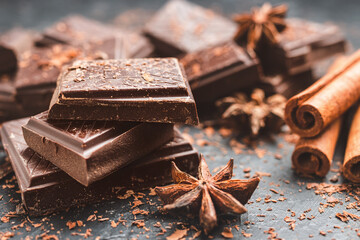 Dark chocolate bar pieces on dark background with grated chocolate and spices, pile chunks of broken chocolate