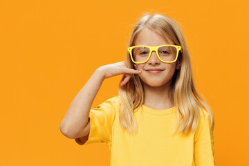 a cute girl, blonde, stands on a yellow background in yellow glasses for vision and shows a phone gesture with her hand