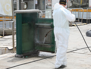 Worker during the cleaning of urban furniture in the city with a jet of a water cleaner