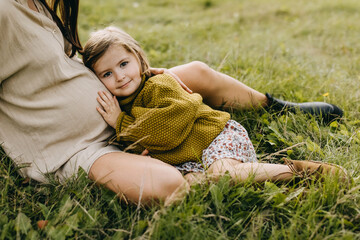Little girl leaning on her pregnant mother belly, hugging, listening to what is inside the belly. Big sister concept.