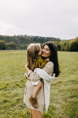 Pregnant woman and her toddler daughter hugging. Mother holding little girl in arms, spending fun time outdoors.