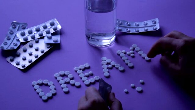A woman with a mental disorder is about to commit suicide by poisoning herself with sleeping pills, folds the word Dream from the pills. Pills on female hands in blue neon light. Overdose and suicide 