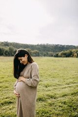 Pregnant woman with long hair, holding hands on belly, outdoors, wearing a warm wool dress.