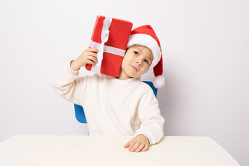 Portrait of a satisfied little child boy in christmas Santa hat. laughing isolated over white background. Holds a gift box. Preparing for the New Year holidays