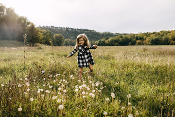 Little girl running in an open field with dandelions, wearing a dress, on a summer day.