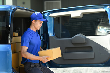 Asian man courier checking information on cardboard box while sitting open delivery van. Shipping and delivery service concept