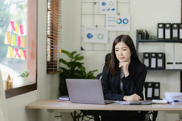 Asian businesswoman working on financial paperwork using laptop online tax, loan, bank debt for mathematical finance on desk, accounting, statistics and analytical research concept.