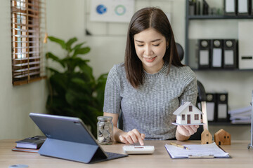 Asian businesswoman holding wooden house, concept of buying and selling house and real estate price, rent, money or home insurance Calculation of a mortgage, loan or investment in real estate.