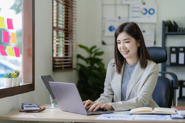 Fototapeta premium Asian businesswoman working on financial paperwork using laptop online tax, loan, bank debt for mathematical finance on desk, accounting, statistics and analytical research concept.