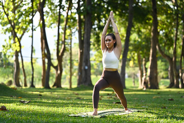 Full length of sporty woman practices yoga, standing in Warrior one pose with nature environment in...
