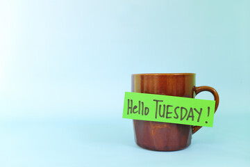 Welcome, hello and happy Tuesday concept. Selective focus of coffee cup with written message isolated in blue background.