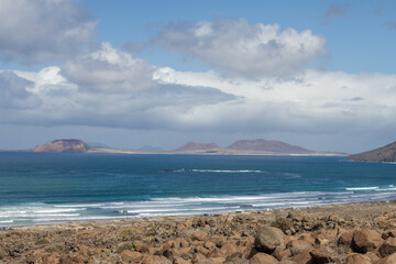 Seascape. Beach with waves. Yellow sand dunes. Ocean. Islets in the background. Blue sky with white fluffy clouds. Famara beach, Lanzarote, Canary Islands, Spain.