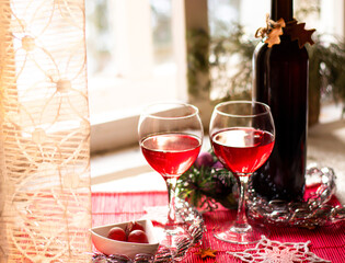 bottle of red wine and two full glasses against light window, festive christmas serving behind a transparent curtain