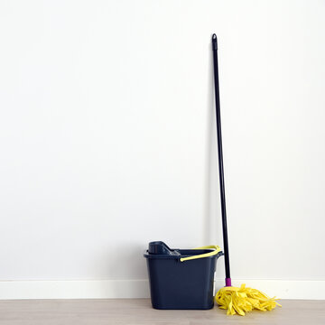 Una fregona y un cubo gris delante de una pared blanca en una habitaci&oacute;n vac&iacute;a.