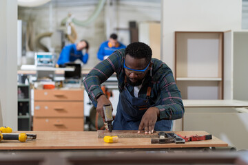 Male carpenter using pneumatic nail gun making new furniture at wood workshop. Production line of...