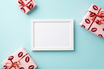 Valentine's Day concept. Top view photo of white photo frame and present boxes in wrapping paper with kiss lips pattern on isolated pastel blue background with blank space