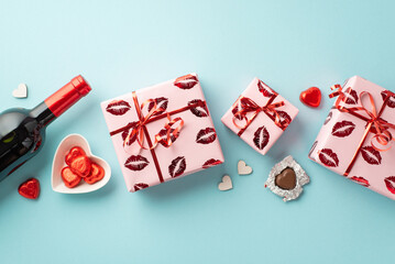 Fototapeta na wymiar Saint Valentine's Day concept. Top view photo of wine bottle gift boxes in wrapping paper with kiss lips pattern and heart shaped saucer with chocolate candies on isolated light blue background