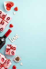 Valentine's Day concept. Top view vertical photo of present boxes wine bottle saucer with chocolate candies and inscription love on isolated light blue background with empty space