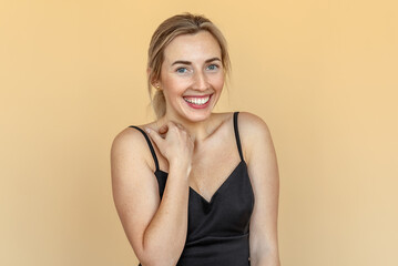 Fototapeta premium Shy, timid, pretty young woman with freckles stands over beige background. Beautiful girl surprised and wondered looks on you. Expressive facial expressions