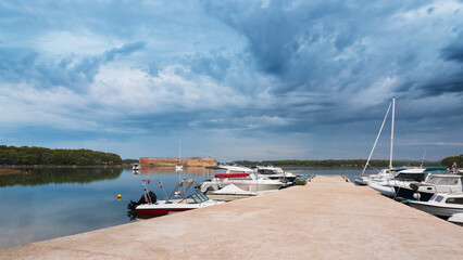 Fototapeta na wymiar Pier with boats on the bay at sveti nikola fortres with dark clouds, sibenik