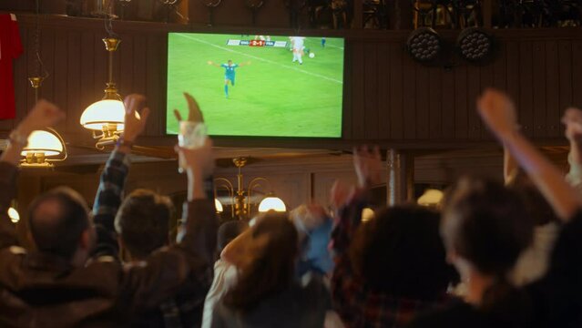 Group of Soccer Fans Watching a Live Football Match in a Sports Bar. People Standing in Front of a TV, Cheering for Their Team. Player Scores a Goal and Crowd Celebrate Winning the Championship.