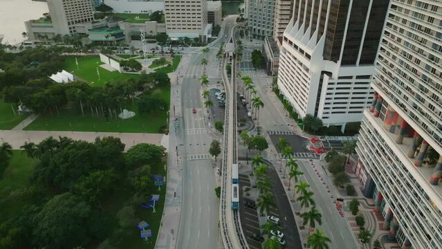 Cinematic aerial shot of subway train moving along the rail track in Miami downtown. High angle drone shot revealing skyscrapers in the background. Following train on monorail. American megapolis.