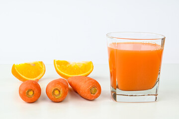 Carrot orange juice in a glass cup  with carrot and orange slices in the background.