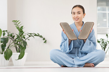Asian woman sitting in lotus position on yoga mat and holding sadhu boards.