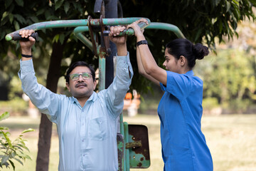 Obraz premium A physiotherapist or professional caregiver watches closely as a senior adult woman exercises on an outdoor gym.