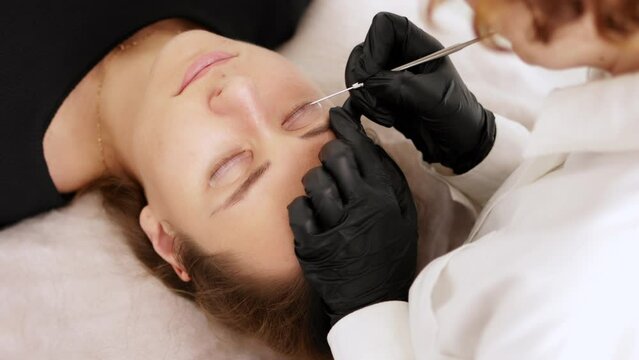 Beautician separates eyelashes with using a special tool with a needle and bends into silicone curlers. Preparation for lamination of eyelashes in a beauty salon.	