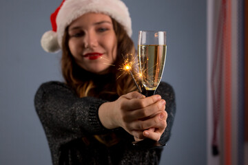 beautiful sparklers and a glass of champagne in a woman hands on gray background. Looks and smiles into the camera, isolated on gray background