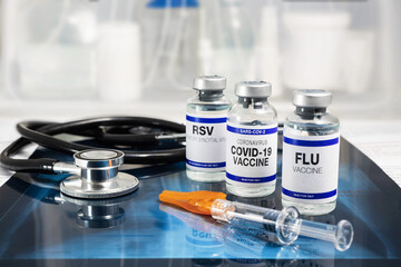 Bottles of vaccine for Influenza Virus, Respiratory Syncytial virus and Covid-19 for vaccination. Flu, RSV and Sars-cov-2 Coronavirus vaccine vials over Radiography pulmonar with stethoscope - obrazy, fototapety, plakaty