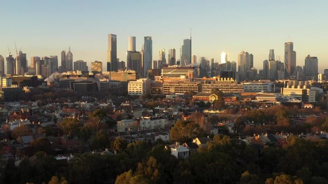 Melbourne city backwards tracking drone aerial showing high rise buildings and Parkville at sunrise, Victoria, Australia