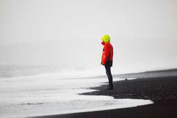 Man in red jacket standing on Reynisfjara beach