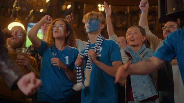 Group of Multicultural Friends Watching a Live Soccer Match in a Sports Bar. Excited Fans with Painted Faces Cheering. Young People Celebrating When Team Scores a Goal and Wins the Football World Cup.