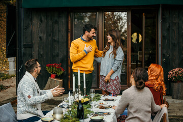 Host couple having a toast and surprising their group of friends at a garden party with positive news. Male and female hosts standing in front of their house.
